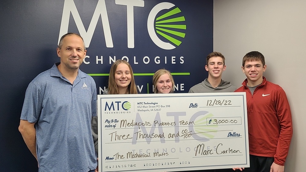 The Mediapolis robotics team holding a giant check in front of an MTC Technologies mural